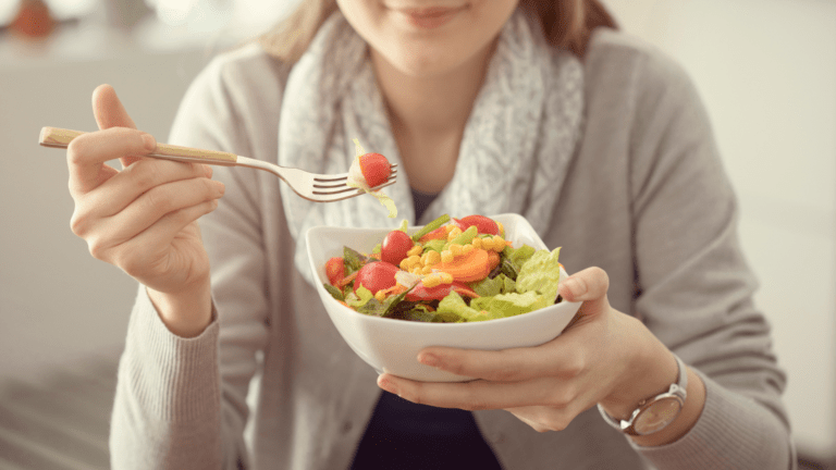A woman holding a bowl of salad as she eats lunch.