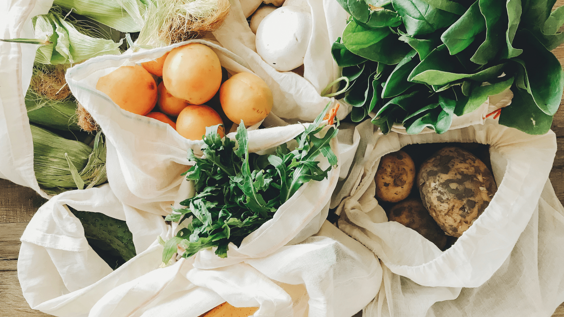 Grocery bags full of fruits and vegetables on a white kitchen counter.