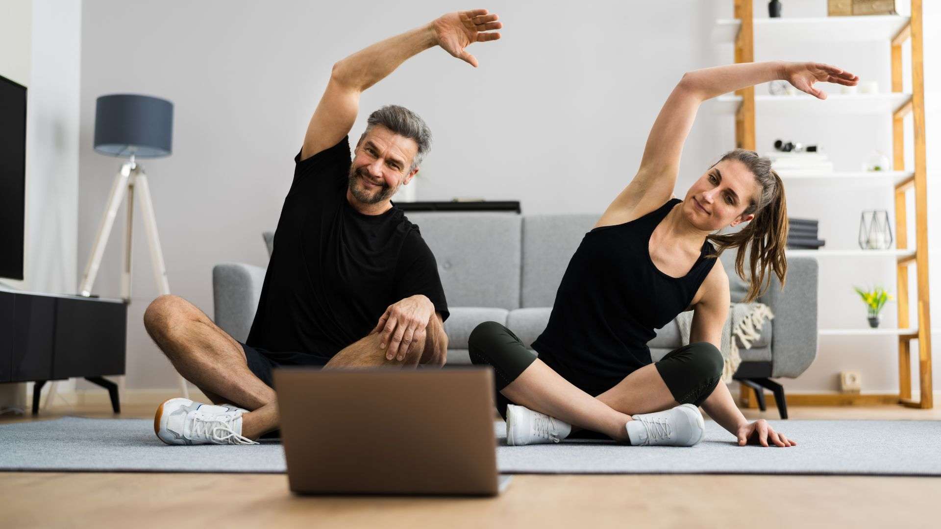 A middle aged couple working out at home to a video on a laptop.