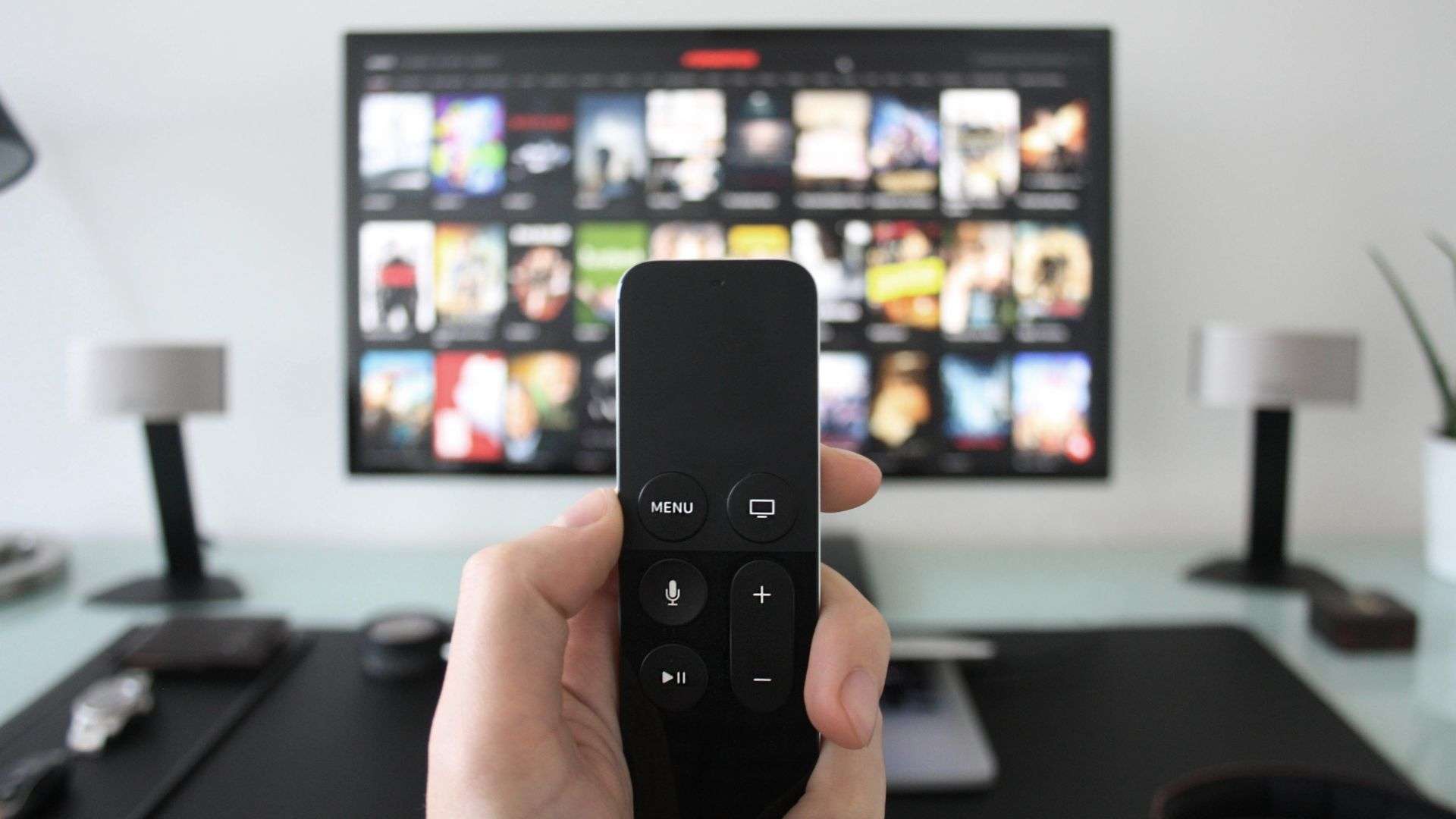 A closeup of a remote with large screen in the background with streaming service menu on it.