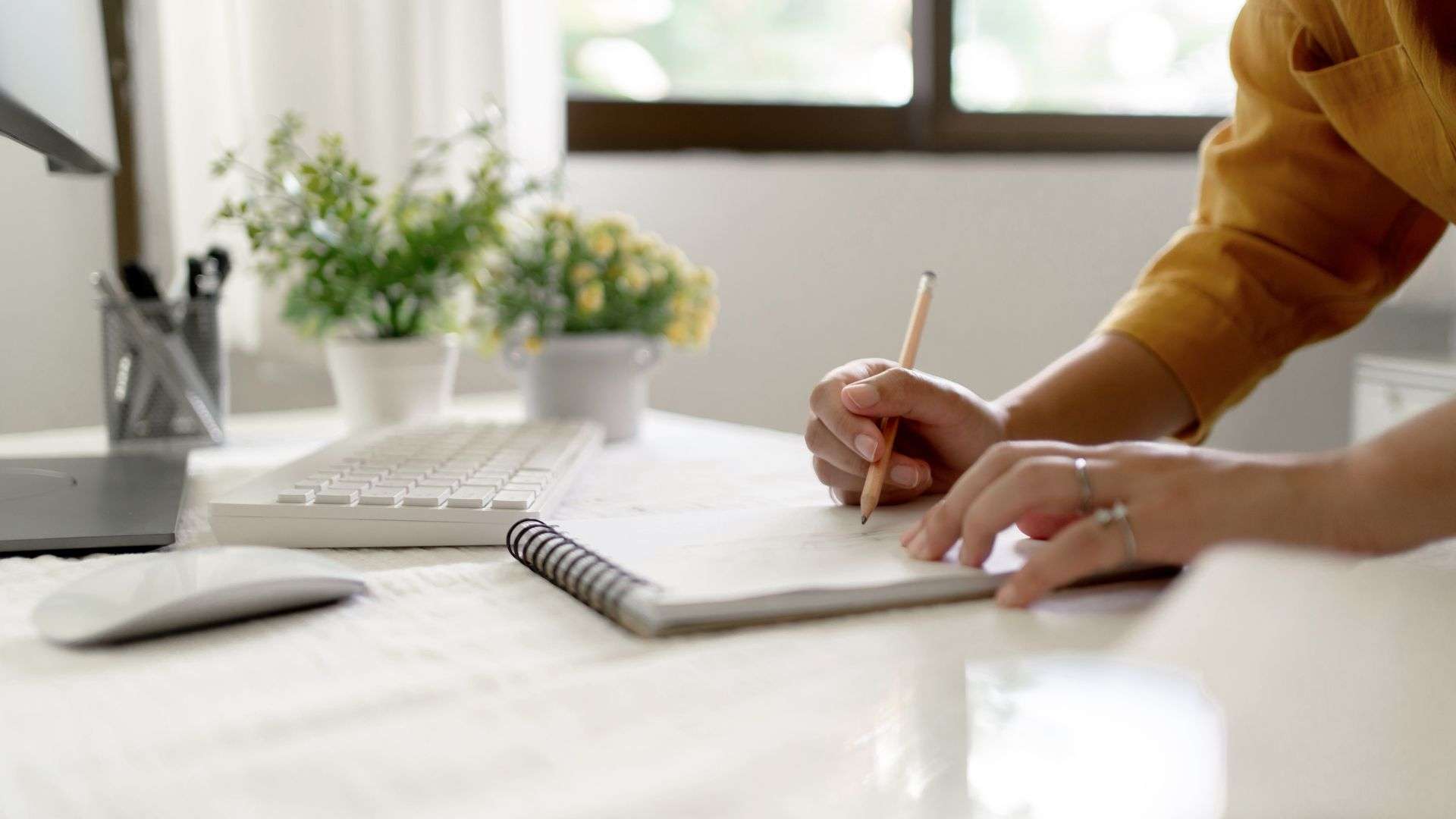 Woman writing in a notebook on clean, uncluttered desk.
