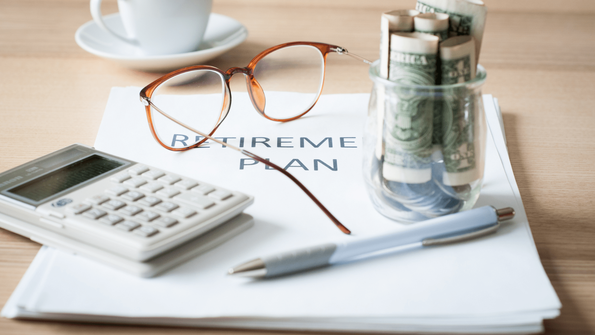 Packet of documents titled "Retirement Plan" on a desk with a calculator, glasses, coffee, and some collected cash.